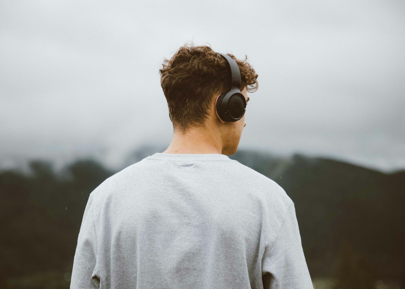 Personne vue de dos, casque sur les oreilles, face à des collines dans la brume