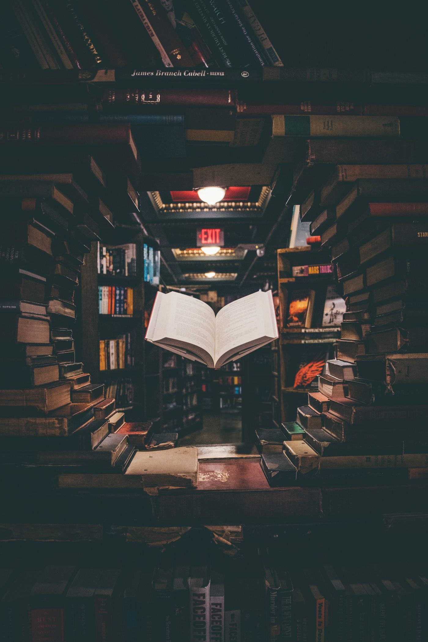 Livre ouvert posé au milieu de piles de livres dans une bibliothèque sombre